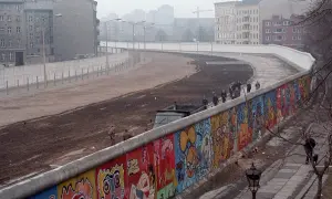 Kolorowy Mur Berliński, świadectwo czasów, kiedy powstał mur berliński, z ludźmi spacerującymi po jego szczycie i budynkami w tle.
