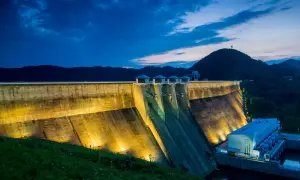 Największa tama w Polsce nocą, oświetlona, z górami w tle.