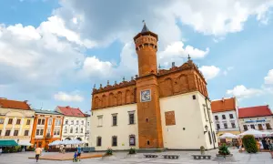 Rynek w Tarnowie z ratuszem i kolorowymi kamienicami. Słoneczny dzień, chmury na niebie.