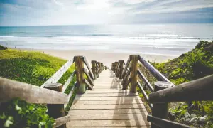 Drewniane schody prowadzące na piaszczystą plażę z widokiem na ocean. Idealne miejsce na wakacje.