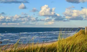 Piękny widok na morze z piaszczystą plażą i wydmami porośniętymi trawą. Na horyzoncie statki, a na niebie chmury. Dźwirzyno atrakcje to idealne miejsce na wypoczynek.