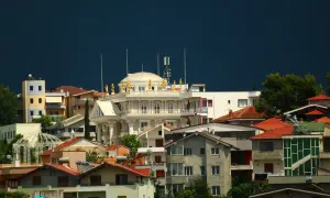 Widok na miasto z białym budynkiem ozdobionym złotymi posągami, przypominającym pałac. W tle ciemne niebo. To nie są stolice Europy, ale malowniczy krajobraz.