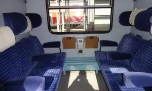 Wnętrze wagonu z niebieskimi siedzeniami. To miejsce dla osób ozn nie na wózku, z wygodnymi zagłówkami i podłokietnikami.