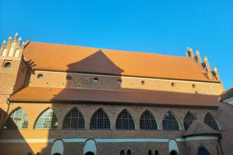 Zamek kapituły warmińskiej w Fromborku, ceglana budowla z pomarańczowym dachem i łukowymi oknami, pod błękitnym niebem.