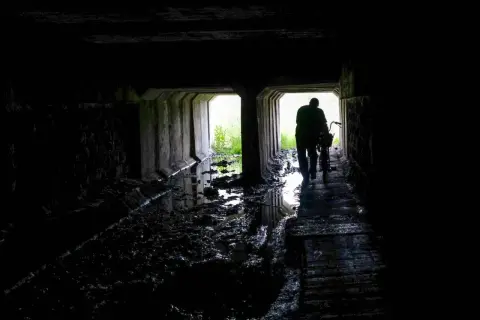 Mroczny tunel, błoto i woda. Postać z rowerem wychodzi ku światłu. Czy to początek drogi przez nawiedzone miejsca w Polsce?
