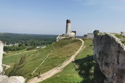 Ruiny zamku na wzgórzu, z wieżą i fragmentami murów. W dole ścieżka, idealna na rowerowe wycieczki po okolicach Częstochowy.