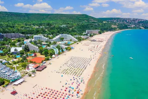 Słoneczny dzień nad morzem w Bułgarii. Tłumy plażowiczów, hotele i zielone wzgórza tworzą malowniczy krajobraz.