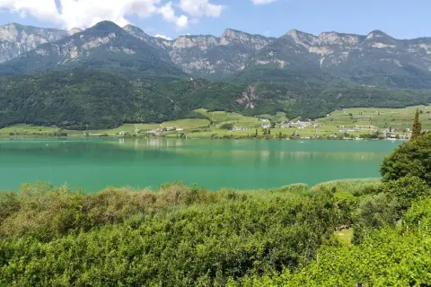 Zielony, spokojny Lago di Caldaro otoczony zielonymi wzgórzami i majestatycznymi górami.