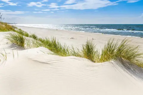 Piękne plaże w Polsce. Biały piasek, trawy na wydmach i spokojne morze pod błękitnym niebem.