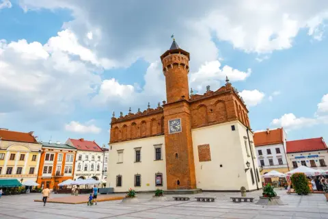 Rynek w Tarnowie z ratuszem i kolorowymi kamienicami. Słoneczny dzień, chmury na niebie.