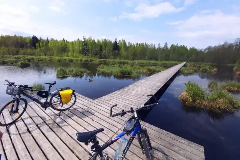 Dwa rowery na drewnianym pomoście nad wodą, otoczone zielenią. Idealne miejsce na odkrywanie tras rowerowych Białystok.
