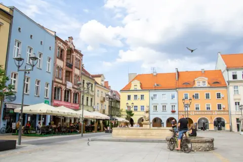 Kolorowy rynek w Gliwicach, idealne miejsce na weekendowe atrakcje. Ludzie siedzą w ogródkach kawiarnianych, a w tle widać zabytkowe kamienice.