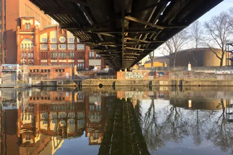 Pod mostem w Berlinie odbija się w rzece ceglana architektura i nagie drzewa.