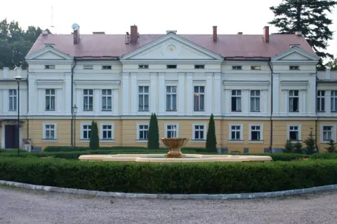 Pałac w Sasinie, z fontanną i zadbanym ogrodem, otoczony drzewami.
