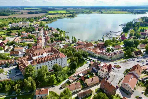 Malowniczy widok na miasteczko nad jeziorem w regionie Warmia i Mazury. Zamek, kolorowe kamienice i przystań jachtowa tworzą urokliwy krajobraz.