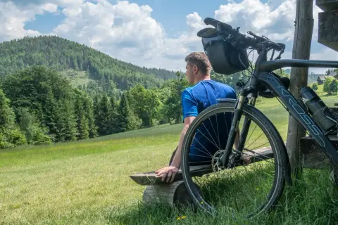 Mężczyzna odpoczywa na ławce po przejażdżce rowerem po Beskidach. Piękny widok na góry i lasy.