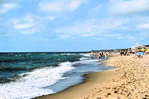 Plaża w Dąbkach tętni życiem. Ludzie kąpią się w morzu, spacerują brzegiem, a na piasku odpoczywają. To idealne miejsce na wakacyjne atrakcje.