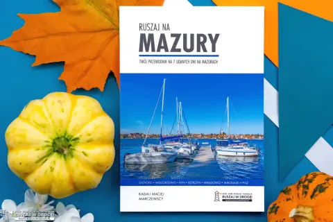 Przewodnik "Ruszaj na Mazury" z widokiem na żaglówki i urokliwe jeziora mazurskie. Jesienne dekoracje dodają uroku.
