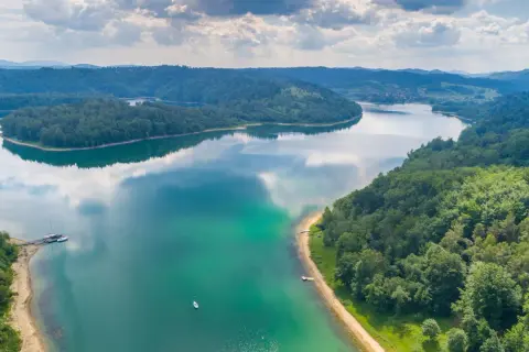 Malownicze jezioro otoczone lasami, z kilkoma łodziami przy brzegu. Idealne fajne miejsca nad jeziorem na wypoczynek.