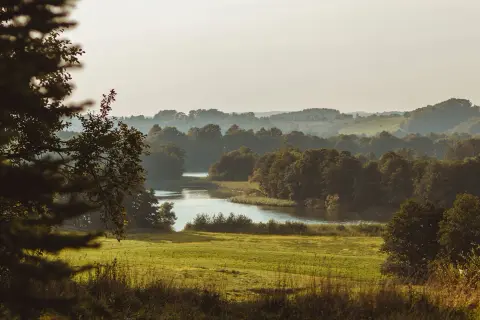Malowniczy krajobraz Kaszubskiego Parku Narodowego z jeziorem, łąkami i lasami w oddali.