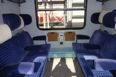 Wnętrze wagonu z niebieskimi siedzeniami. To miejsce dla osób ozn nie na wózku, z wygodnymi zagłówkami i podłokietnikami.