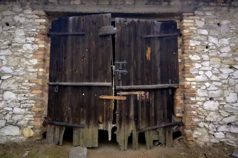 Stare, drewniane wrota do stodoły w Żarkach, zniszczone przez czas, stoją w kamienno-ceglanej ścianie.