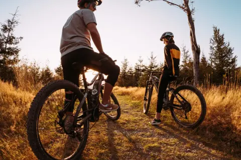 Dwie osoby na rowerach górskich odpoczywają na ścieżce wśród traw. Idealne miejsce na odkrywanie tras rowerowych Śląsk.