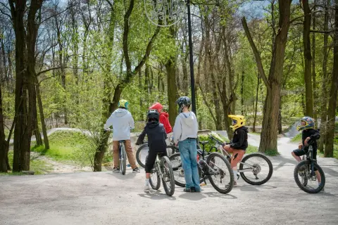 Grupa dzieci w kaskach odpoczywa na rowerach na bielszowice trails. W tle widać leśną ścieżkę rowerową.
