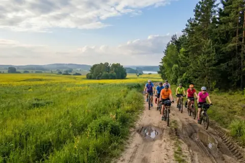Grupa rowerzystów przemierza malownicze **olsztyńskie trasy rowerowe** wśród pól rzepaku i lasów.