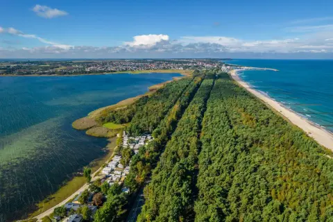 Malowniczy cypel na Helu z lasem sosnowym, plażą i Zatoką Pucką. Widoczny kemping i miasteczko w oddali.