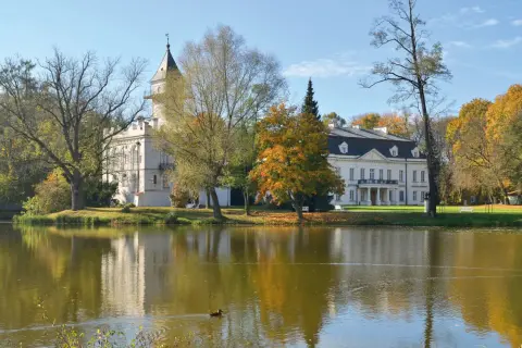 Pałac w Bolimowskim Parku Krajobrazowym odbija się w stawie, otoczony jesiennymi drzewami.