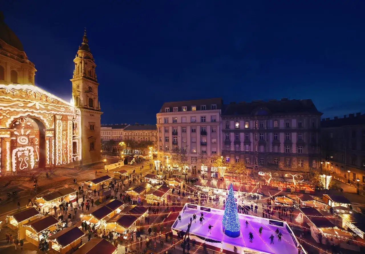 Magiczny budapeszt jarmark bożonarodzeniowy. Tłumy ludzi na lodowisku i przy straganach, oświetlona bazylika w tle.