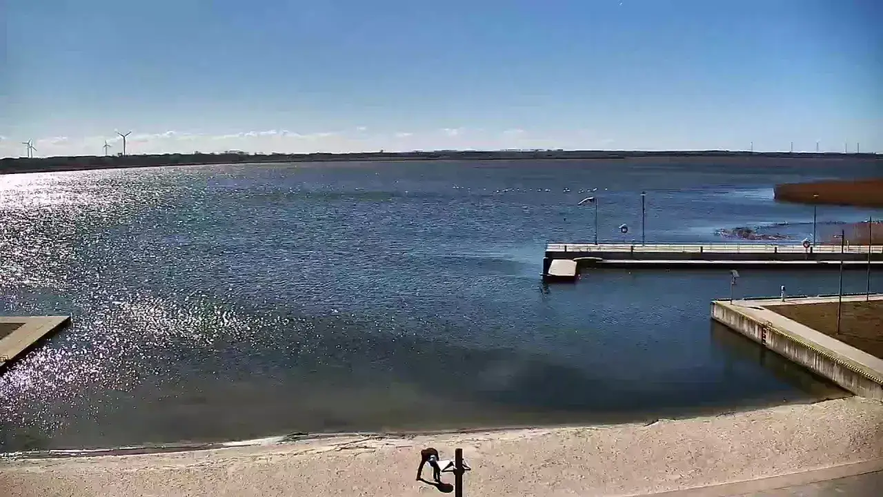 Spokojny dzień nad jeziorem, wiatr obraca turbiny, a na plaży w Dźwirzynie widać pierwsze atrakcje.