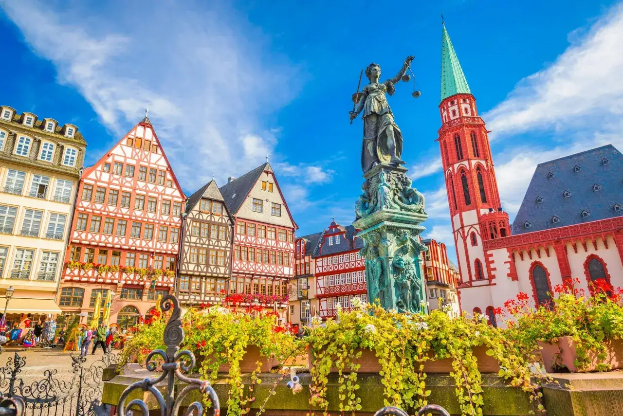 Urokliwy plac w Frankfurcie nad Odrą z zabytkowymi kamieniczkami, fontanną Sprawiedliwości i czerwoną wieżą kościelną.
