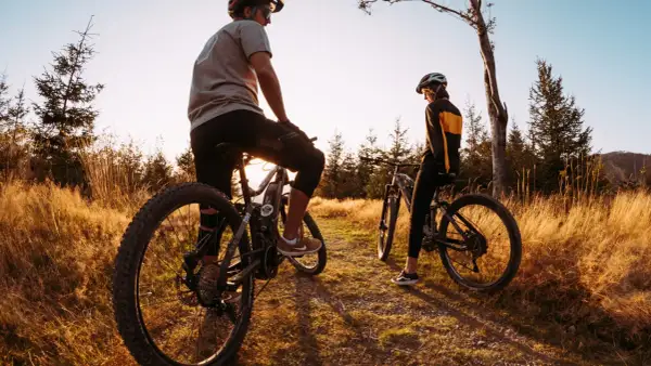 Dwie osoby na rowerach górskich odpoczywają na ścieżce wśród traw. Idealne miejsce na odkrywanie tras rowerowych Śląsk.